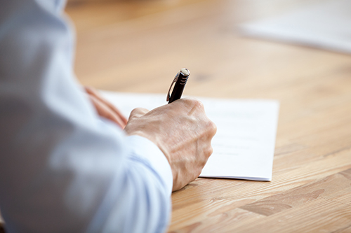 En hand som håller en penna och fyller i ett formulär.