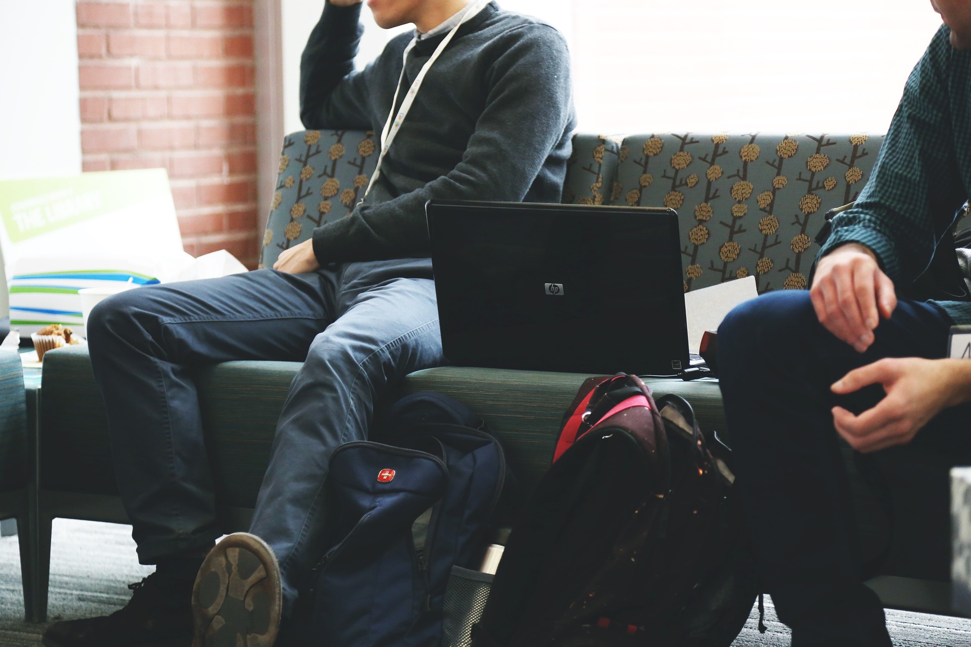 Studenter sitter i en soffa med laptop och ryggsäckar. 