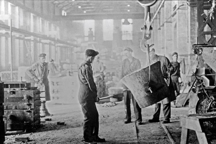 Factory workers in JMW are handling a big pot. The photo is black and white.