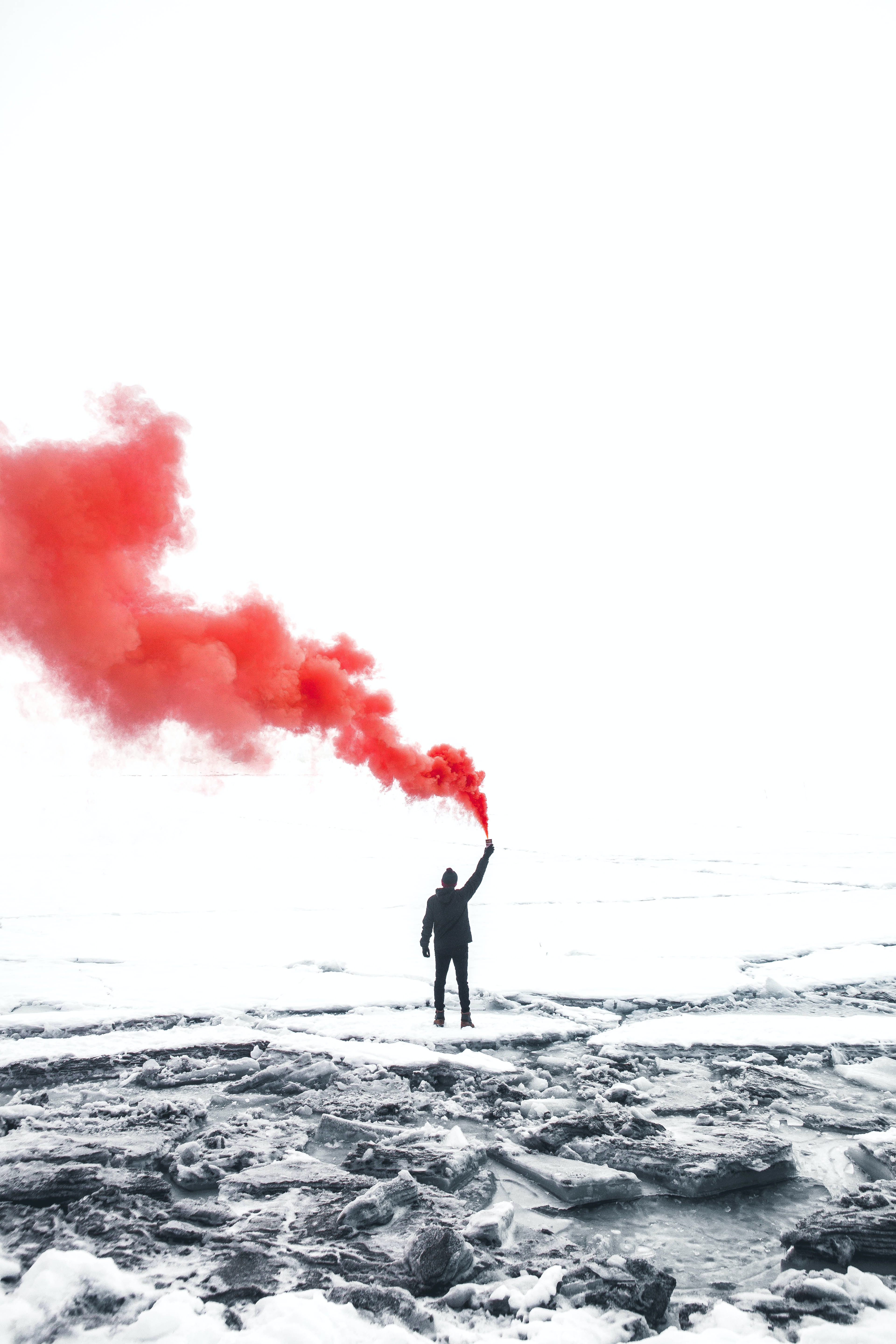 Person som står på klippor vid havet och håller i något som avger röd rök.