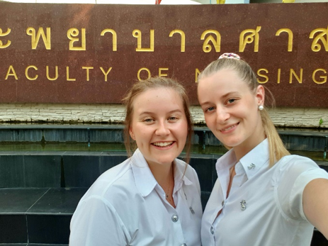 Two girls in front of sign "Faculty of nursing"