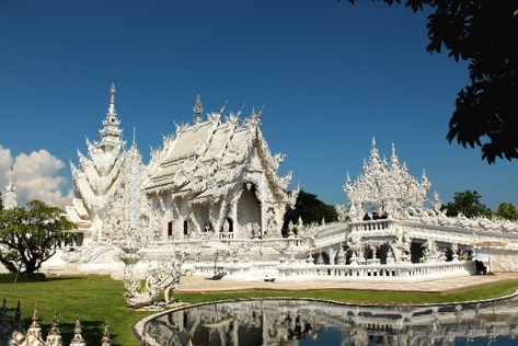 White temple with a pond and some grass in front of it