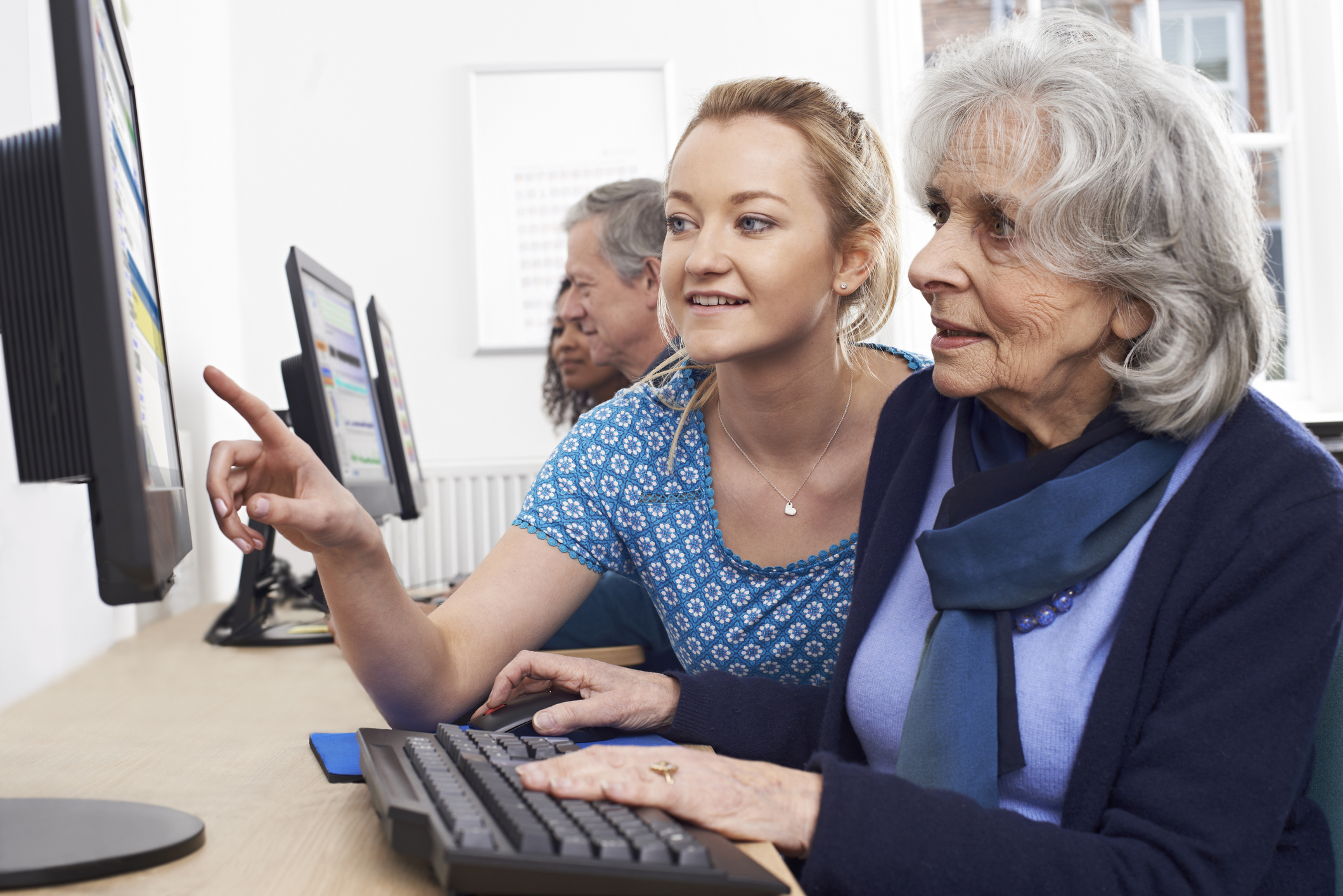 Young female tutor helps elderly woman in a computer class. 