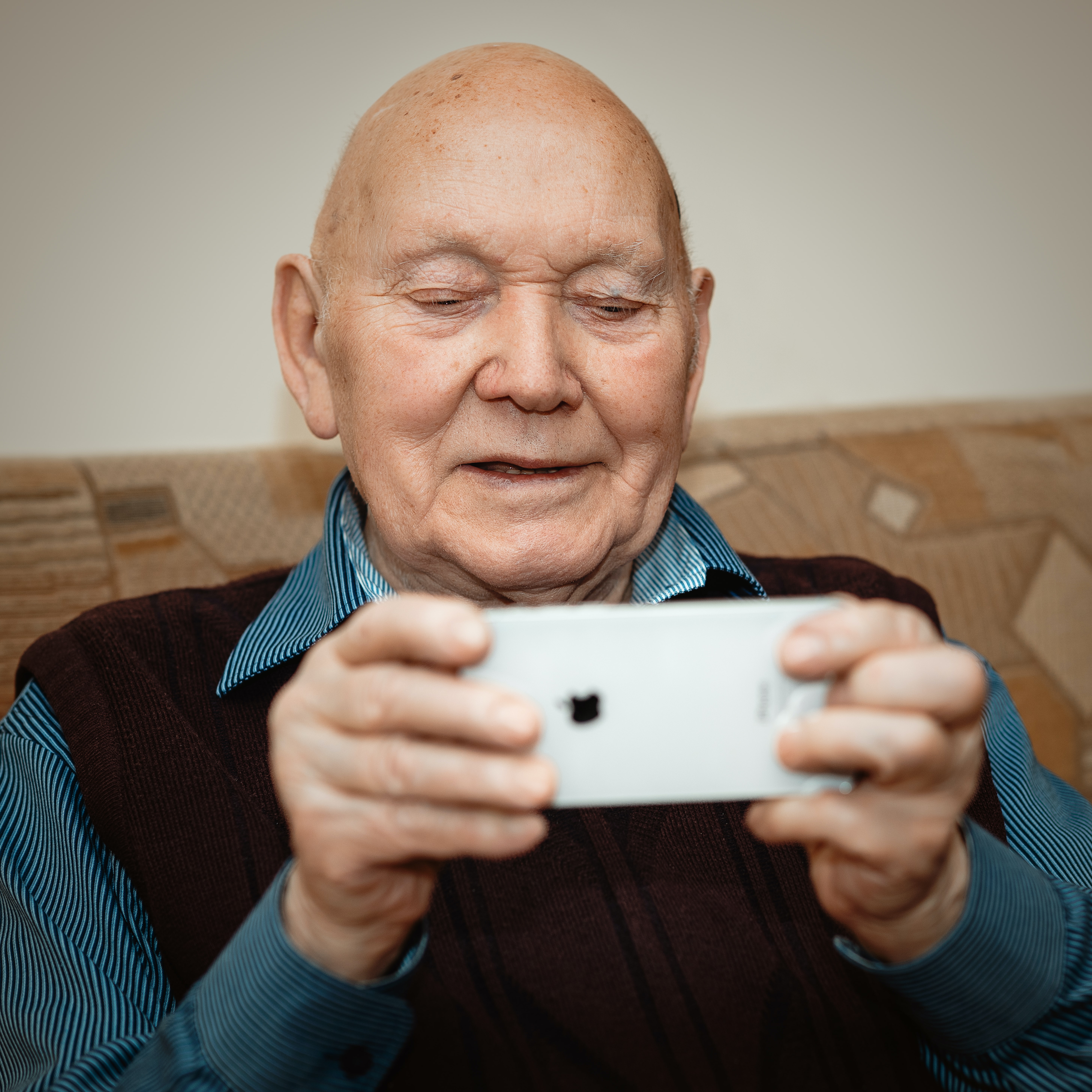 Old man holding up and looking at an iphone. 