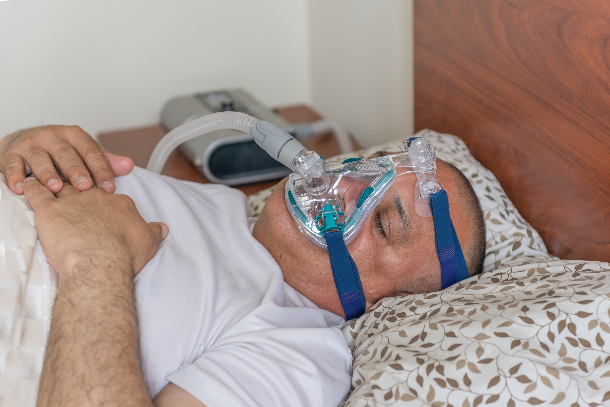 Man som lider av sömnapné, ligger och sover på rygg i sängen med en CPAP -behandlingsmask i ansiktet.