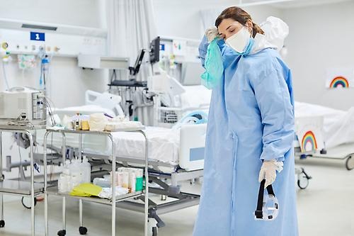 Tired healthcare worker wiping sweat in ICU. She is in protective coveralls after surgery.