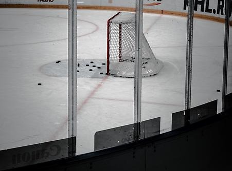 Empty corner of an ice hockey rink with goal. Several hockey pucks are lying on the ice in and outside the mouth of the goal. 