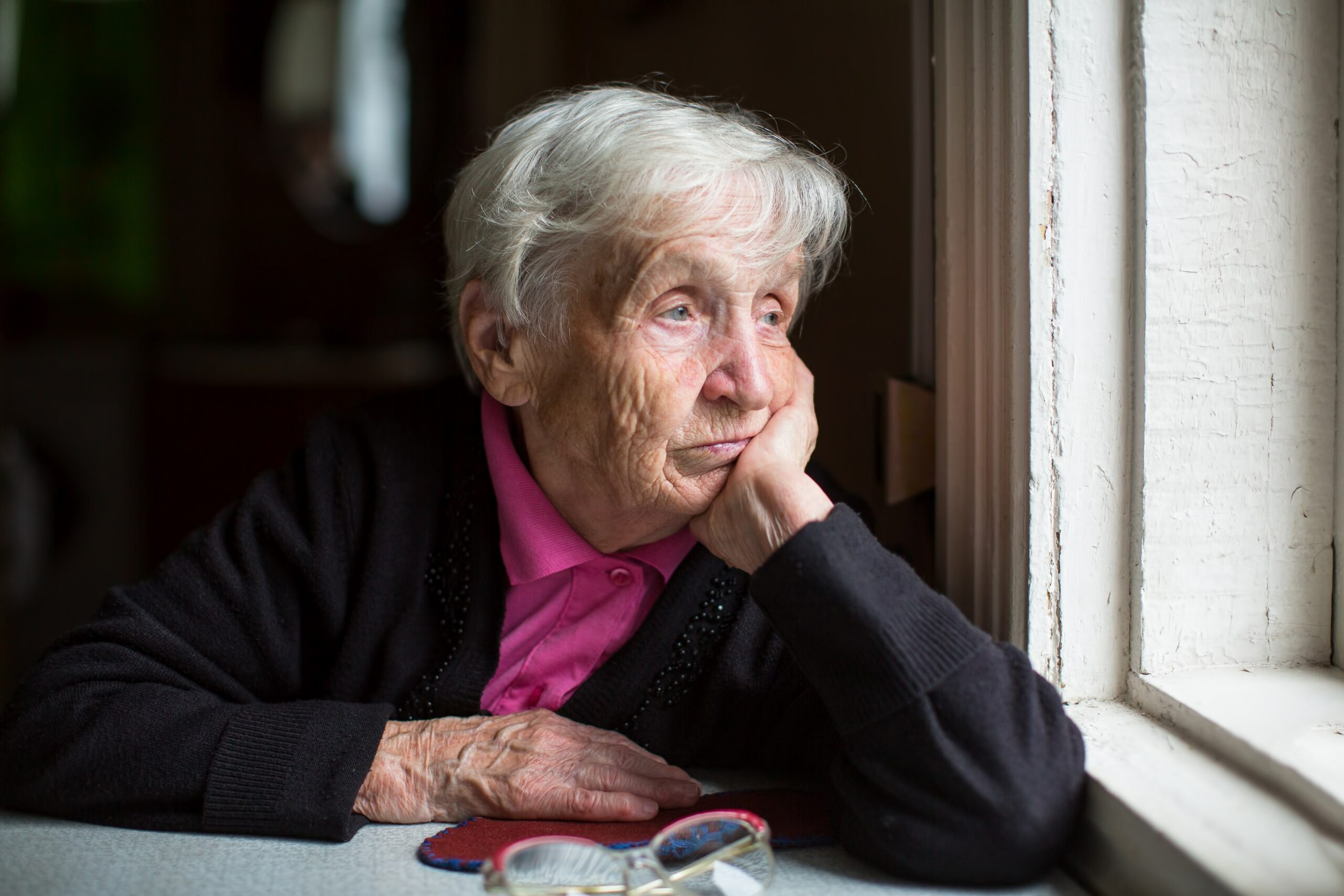 Äldre kvinna som sitter ensam och tittar ut genom ett fönster