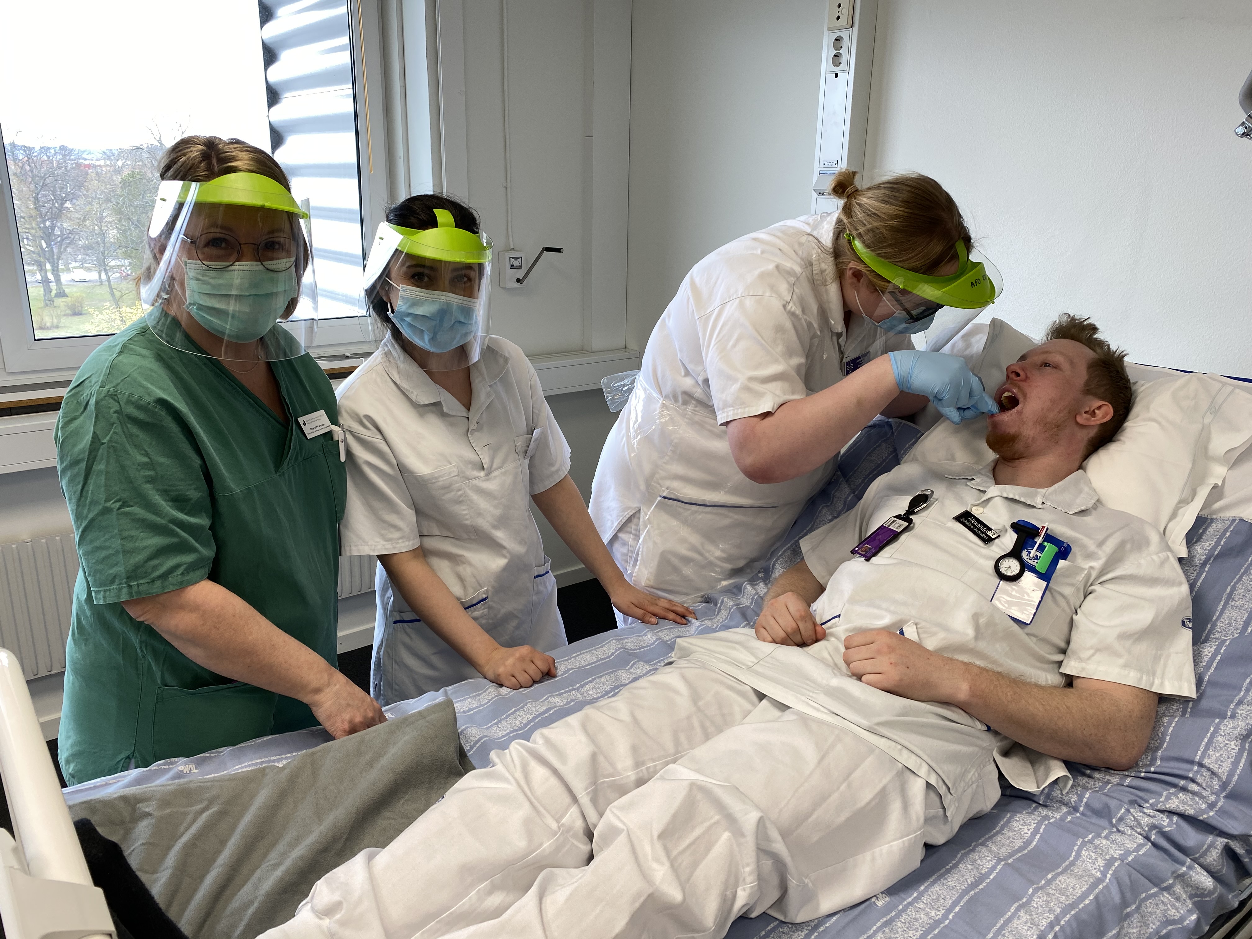 Undervisningsmoment där tre studenter syns tillsammans med en lärare, en av studenterna ligger i en sjuksäng och får tänderna borstade av en annan. 