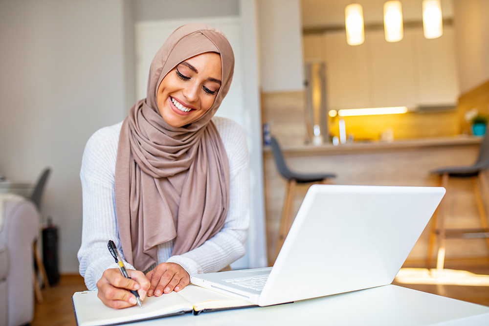 A veiled muslim woman sits at an outdoor table, working on her laptop. 