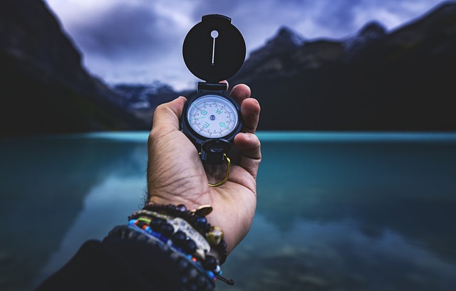 En hand håller i en kompass, i bakgrunden en sjö och berg.