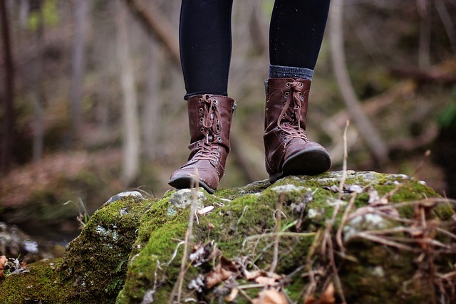 Någon står med ett par läderkängor på en sten i skogen. 