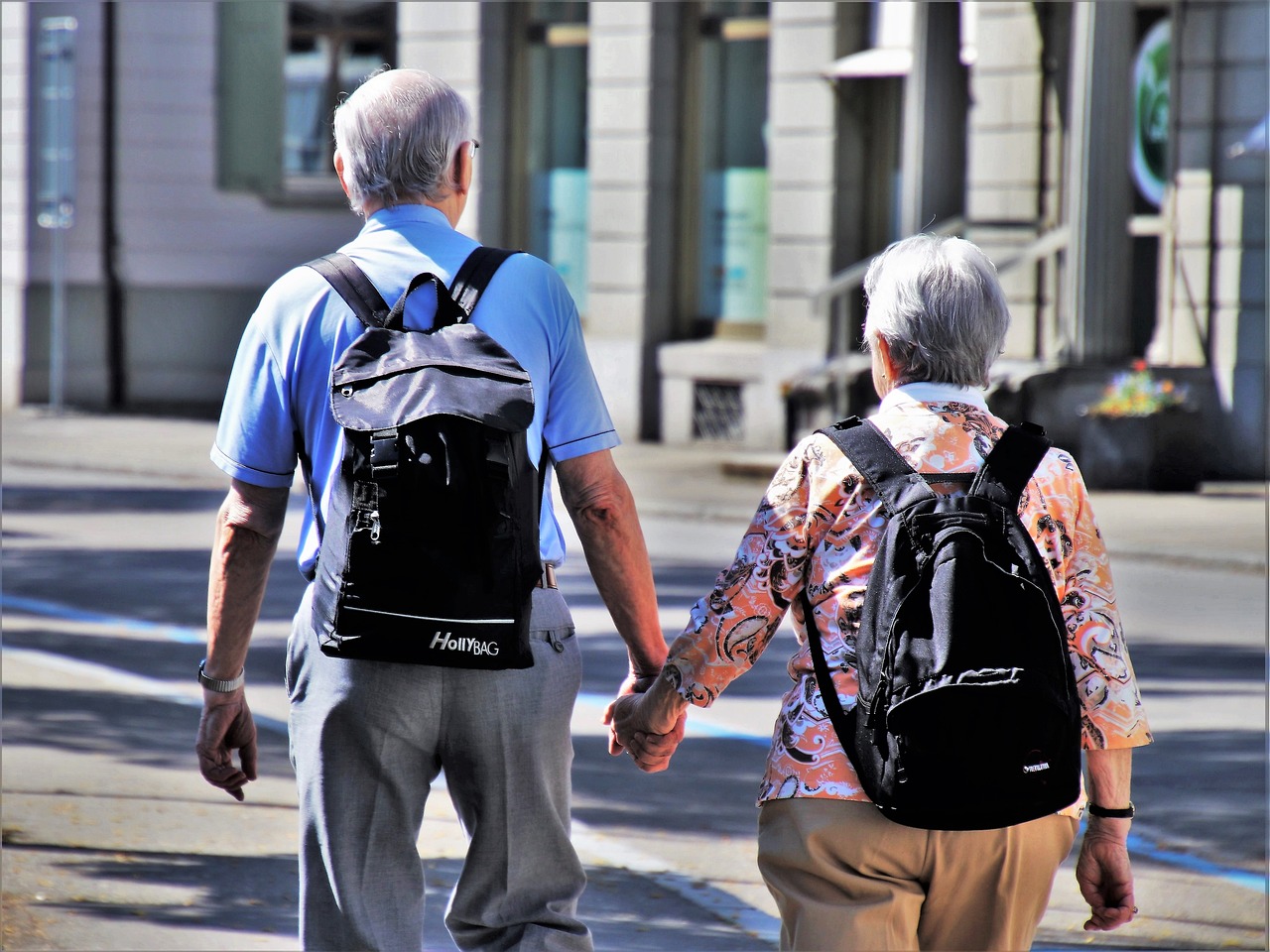 Två äldre personer går hand i hand, med ryggsäckar.