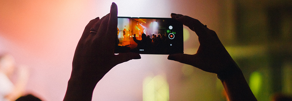 Händer som håller upp en mobil och filmar en konsert