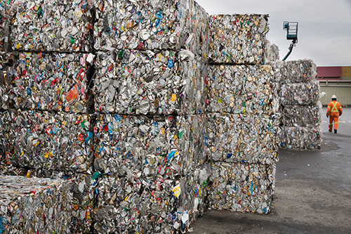 An unidentified worker, at a recycling collection facility, walks past stacks of metal cubes made from crushed tin cans, that await shipping to a recycling plant.