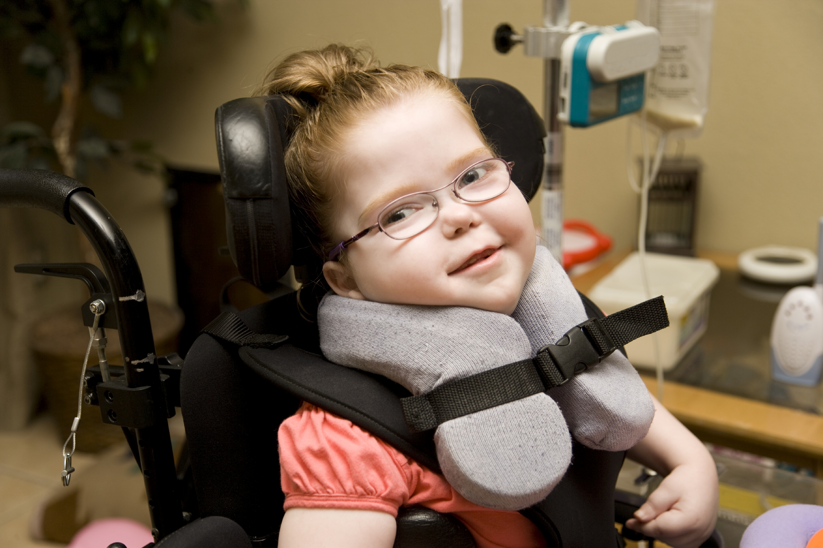 Glad och mycket fin liten flicka med funktionsnedsättningar som sitter i en rullstol.