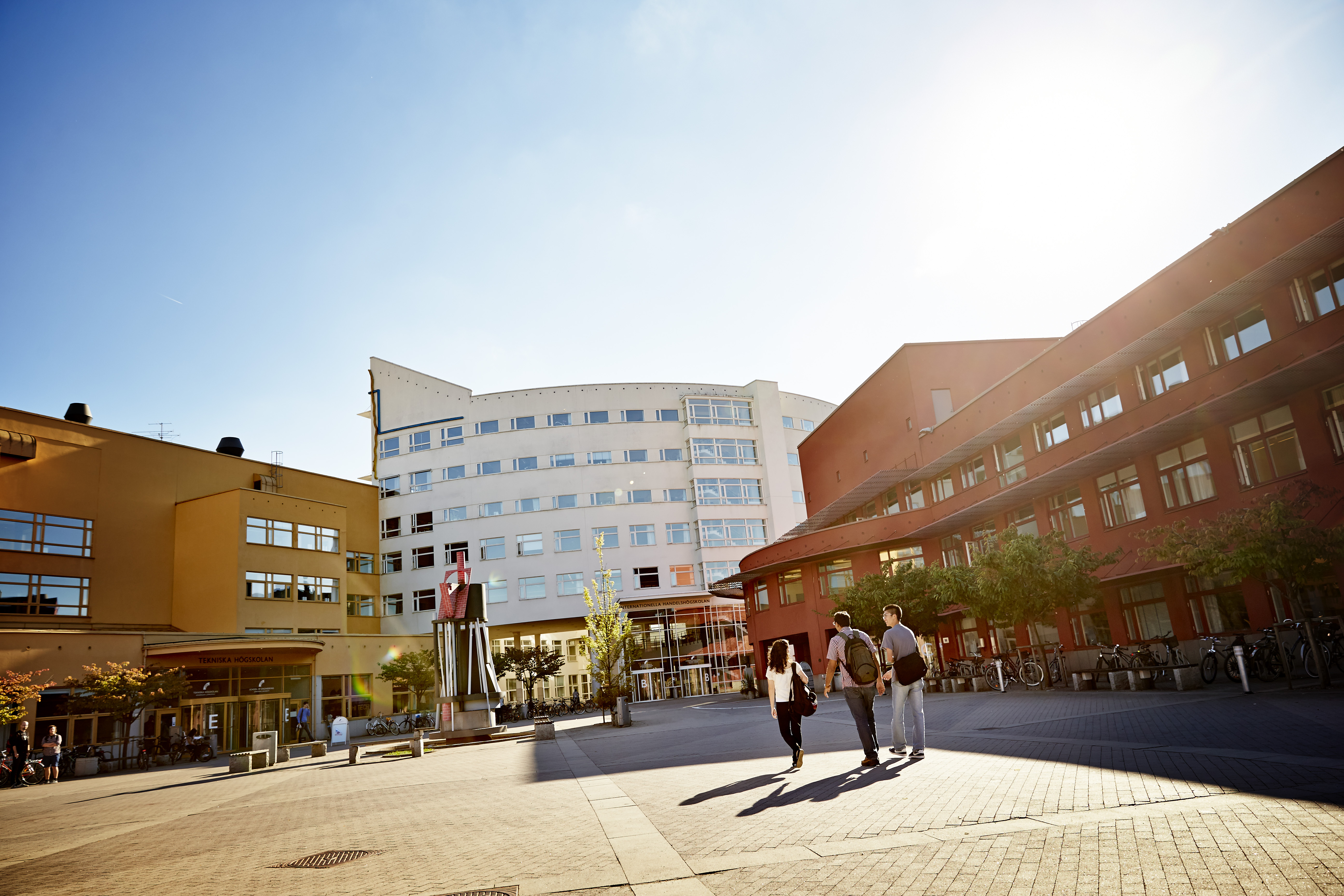 Tre studenter på campus en solig dag