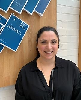 Cinzia Sansone stands next to a wooden board where thesis are nailed. 