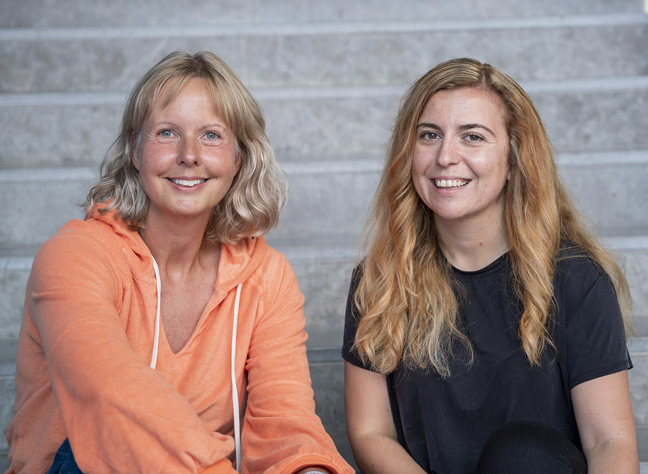 Charlotta Mellander sits to the left and Orsa Kekezi sits to the right. Both are sitting on the steps in JIBS' entrance hall. 