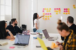 woman-placing-sticky-notes-on-wall-of-boardroom