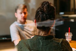 View of the back of a woman sitting at a table opposite a man. 