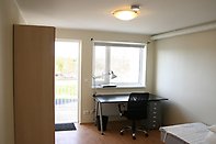 Student dorm room with bed, desk and bookshelf